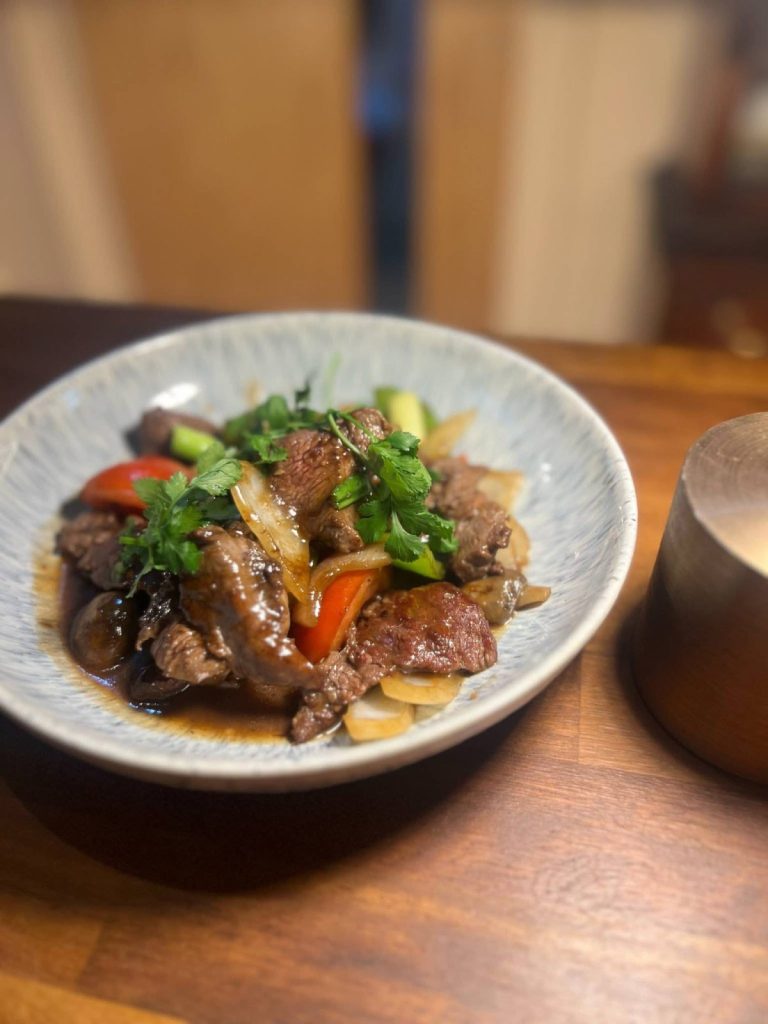 A bowl of beef stir fry with peppers, onions and fresh coriander