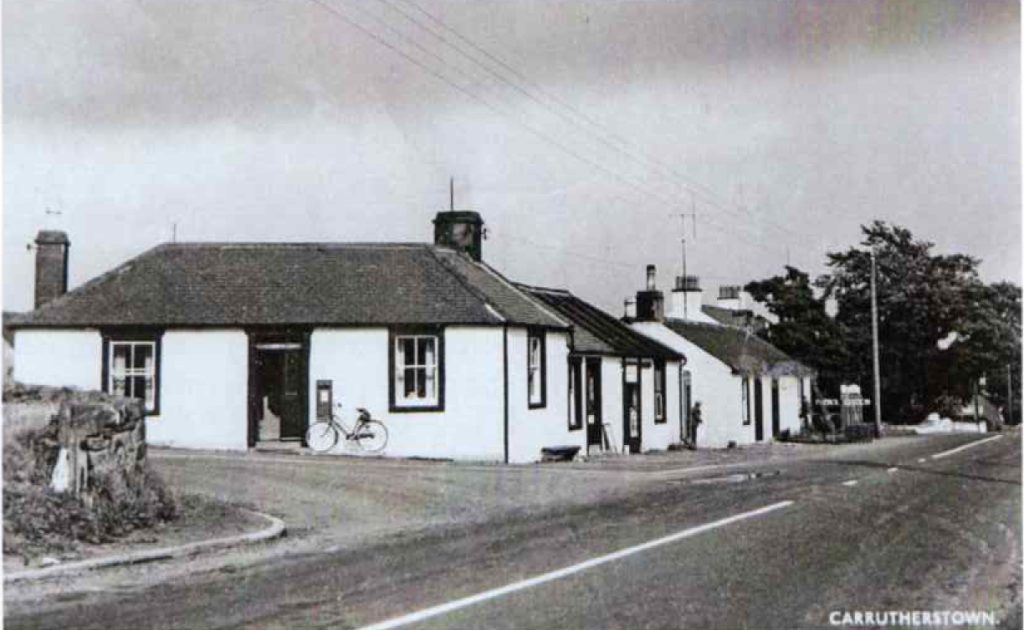 An old black and white postcard of Carrutherstown: a row of white harled single storey cottages along the road, a bicycle leaning by a door