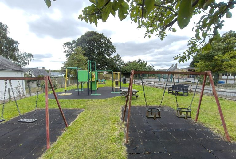 The Carrutherstown playpark, with swings, a climbing frame and picnic benches on the grass