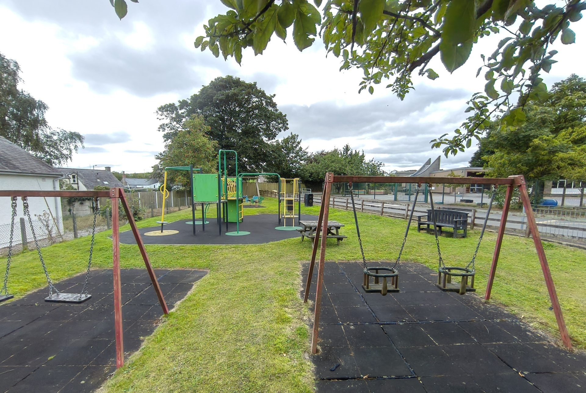 The Carrutherstown playpark, with swings, a climbing frame and picnic benches on the grass