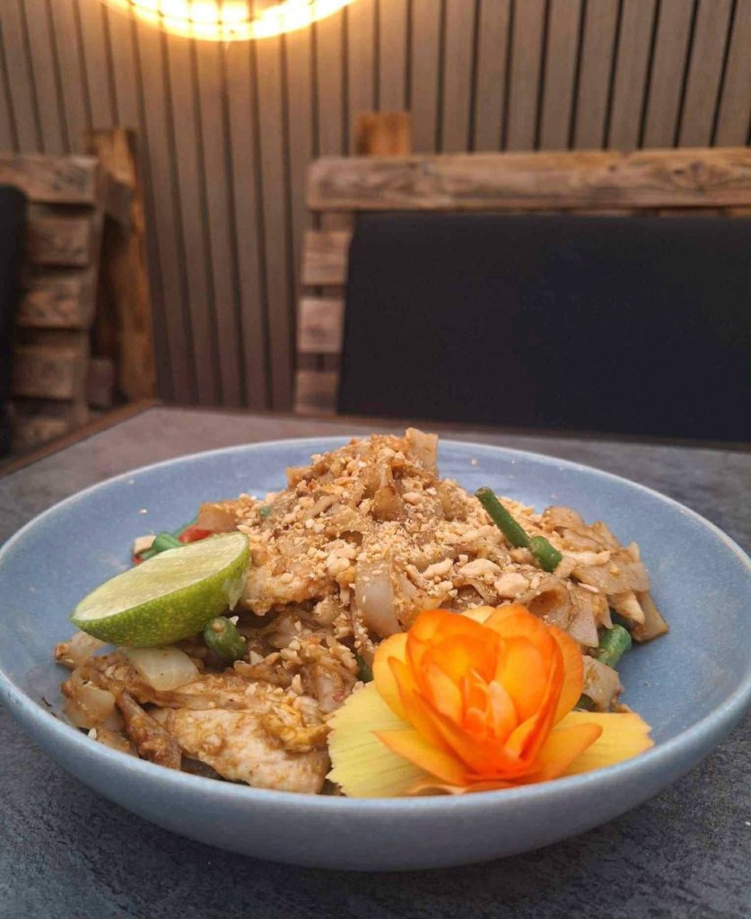 A bowl of pad thai topped with crushed peanuts and a lime wedge