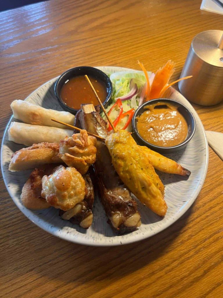A mixed starter platter with spring rolls, ribs, chicken skewers and two dipping sauces
