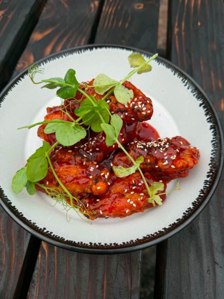 A plate of sweet chilli chicken with sesame seeds and fresh pea shoots